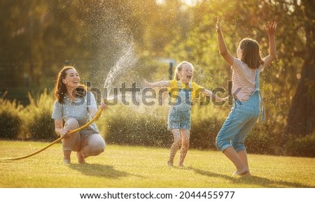 Happy family playing in backyard. Mother sprinkling her kids in hot summer day. Royalty-Free Stock Photo #2044455977