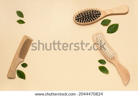 three different wooden combs on a beige background with green leaves with a place for text Royalty-Free Stock Photo #2044470824