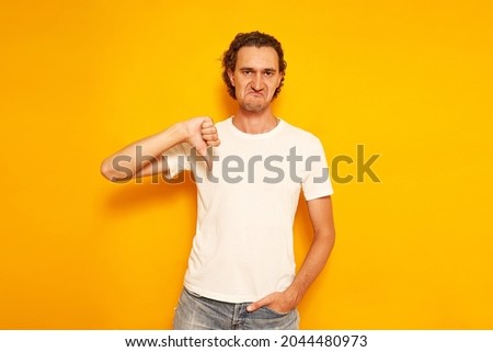 man in casual clothes with a dissatisfied face shows a thumb at bottom as a sign of poor quality denial. insulated on yellow background with space for text. concept of people, service, evaluation