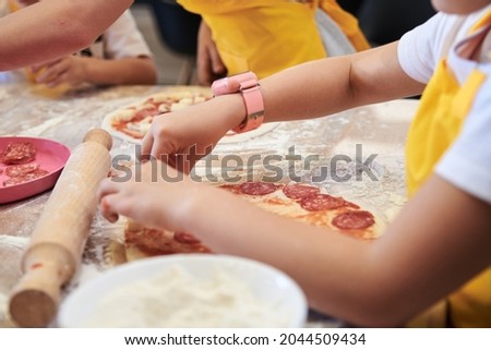 Child wearing yellow apron, putting ingredients dough on the table. Close-up picture of hands, making topping for pizza. Bakery master class for small children. Pizza workshop at juniors' party.