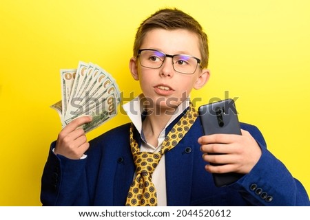 Successful and rich child taking a selfie with money, portrait of a boy in a suit on a yellow background. new