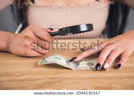 woman examines the money with a magnifying glass. counterfeit check concept
