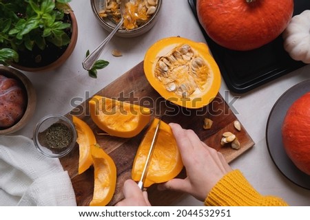 Fresh pumpkin. Cutting pumpkin in slices on cutting board, female hands preparring autumn foods. Baked squash or butternut, top view.