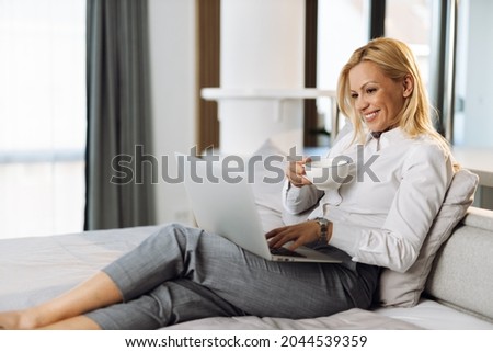Businesswoman drinking coffee while working on laptop in a hotel room