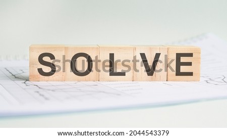 solve is written on light wooden blocks. the word is located on a sheet with charts and graphs. business concept. gray background
