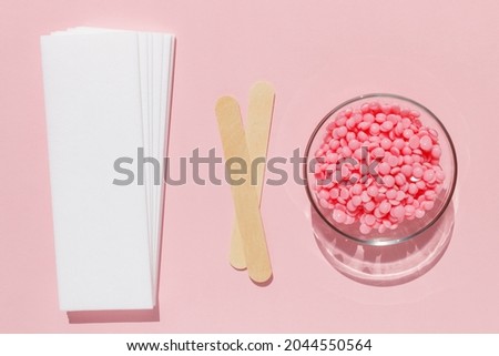 Beautiful pink depilatory wax granules, strips for depilation and wooden spatulas on a pink background. Epilation, depilation, unwanted hair removal. Top view. Royalty-Free Stock Photo #2044550564