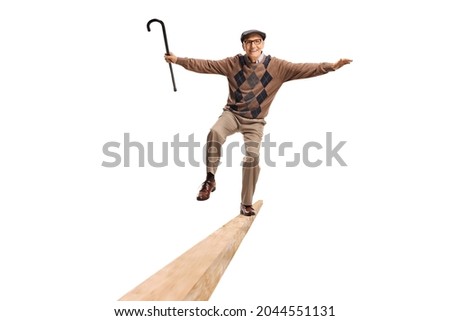 Full length shot of a senior standing on a wooden beam and keeping balance with a walking cane in his hand isolated on white background