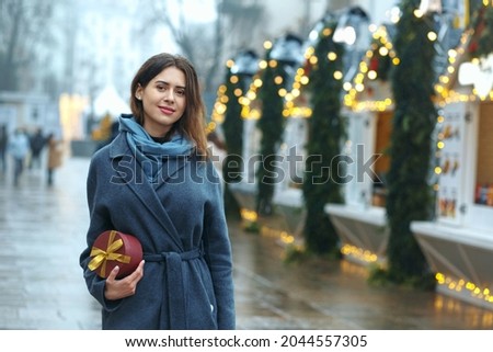Lovely brunette woman holding gift box near the christmas fair. Space for text