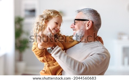 Elegant loving caring grandfather looking at his cute little granddaughter, adorable child girl and positive grandpa holding hands while dancing together in living room at home. Family concept Royalty-Free Stock Photo #2044560683