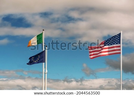 National flag of Ireland and Euro Union in focus. Waving flag of United States of America out of focus on blue color cloudy sky .International relationship theme