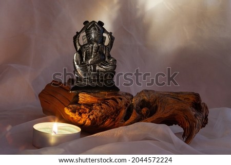 Hindu god Ganesha on dark background. Statue on wooden postament with a smoke of incense and a candle. Copy space.