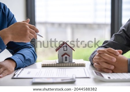 House model with real estate agent and customer discussing for contract after signing contract to buy house with approved property application form insurance or loan real estate background.