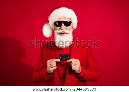 Photo of santa claus hold plastic debit card promoting online payment wear sunglass x-mas hat suit on red color background