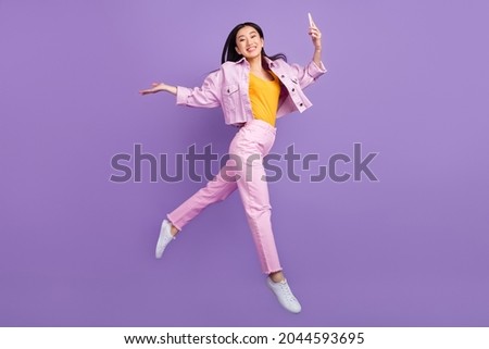 Full size profile photo of funky young brunette lady jump hold telephone wear jacket jeans sneakers isolated on violet background Royalty-Free Stock Photo #2044593695