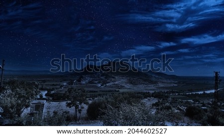Old ancient castle on the hill at night. Rocky peaks of the ridge in the distant background in full moon light and cloudy sky. Adana, Turkey