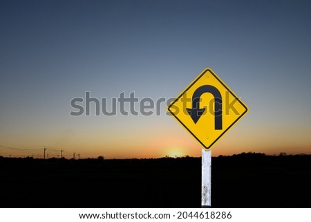 Traffic sign: Left U-turn sign on cement pole beside the rural road with the sunset background, copy space.