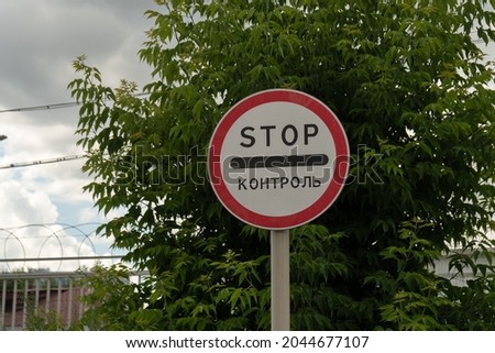 A road sign near the fence with barbed wire, prohibiting entry into the territory with the inscription in Russian - Control, against the background of a maple tree.