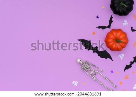 Halloween border made of colorful pumpkins, skeleton and bats on a purple background. Happy halloween concept with place for text. Flat lay.