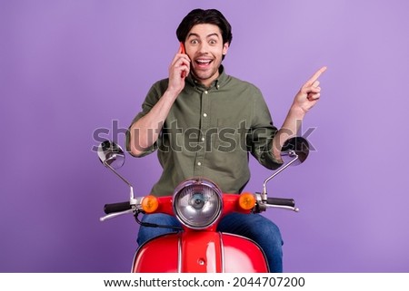 Photo of amazed brunette man point finger empty space talk phone wear jeans isolated on violet color background