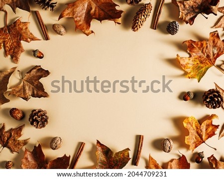 Frame of dry autumn maple leaves, cinnamon sticks, acorns, and pine cones on pastel beige background. Creative fall concept. Minimal natural border with copy space for text. Flat lay.