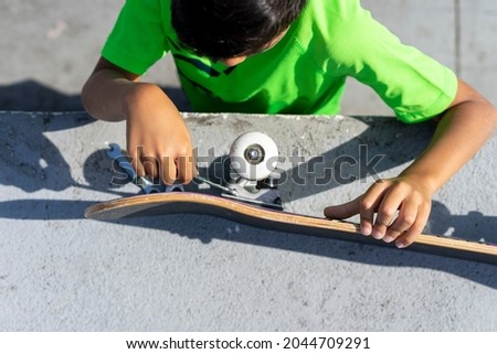 Top view of a boy repairing the wheel of his skateboard after using it inside the skateboard park on a sunny day. High quality photo