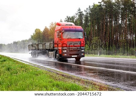 A red flatbed semitrailer tractor driving on the road in rain and poor visibility in summer. Poor visibility concept in bad weather, logistic