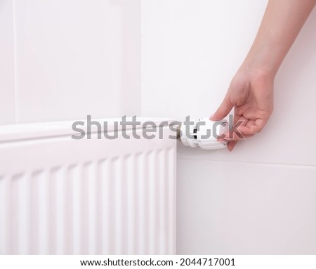 A woman's hand holds the heating thermostat handle. Heating service cost concept, utility price increase Royalty-Free Stock Photo #2044717001