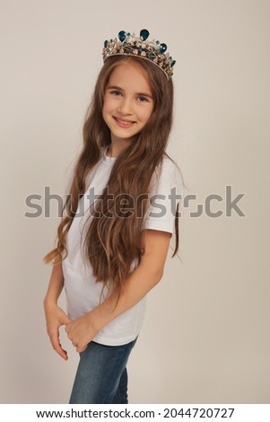 a beautiful sweet happy girl with long hair in a white T-shirt with a crown on her head
