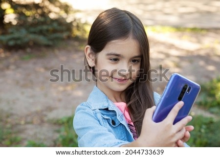 Happy child girl with long dark hear using phone outdoors. 