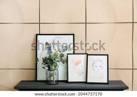 Vase with eucalyptus branches and pictures on fireplace in room