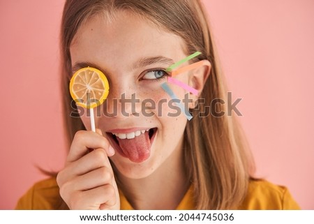 Girl hiding her eye behind sweet candy and looking away while posing to the camera