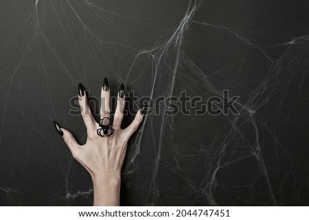 Hand with long black nails and spider ring on a black background with cobwebs. Happy Halloween holiday concept.