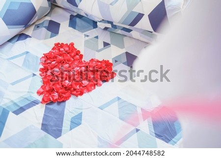 Red rose petals arranged in a heart shape on a couple's bed.