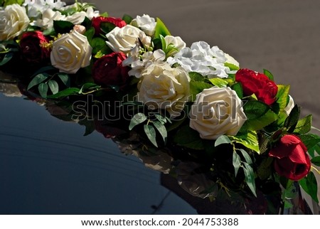 White wedding flowers attached to a black car. Wedding floristics and decorations close up. Wedding and holiday concept.