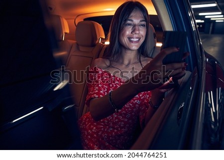 Joyful woman sitting in automobile and using smartphone
