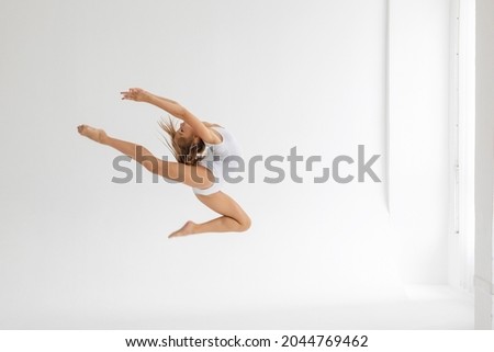 slim artistic teenager girl in white leotard trains on white background in rhythmic gymnastic exercise, children's professional sports