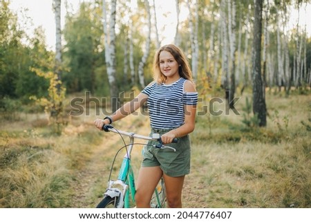 Portrait of a young girl with a blue bicycle. Girl in the woods on a bicycle. Striped T-shirt and dark green shorts. Cycling in the woods