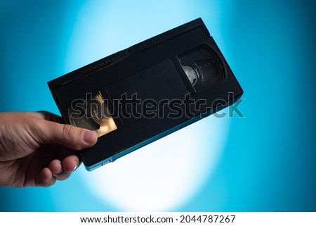 Hand holds retro HVS video cassette on a blue background. Retro wave. 80s 90s
