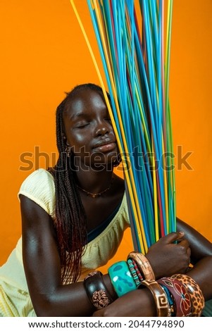 young african girl with closed eyes playing with long colorful drinking straws. Studio shot on yellow background 