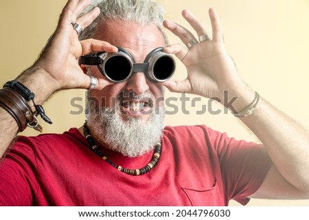 Funny expression of an adult male hipster with melting goggles, bearded man with grey long curly hair collected in a tail, original person