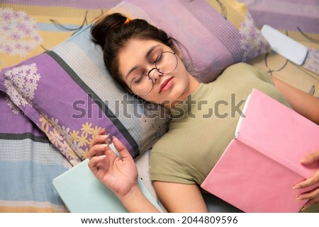 Indoor high angle images of beautiful Asian, an Indian girl student wearing round eyeglasses falling into deep sleep while reading a book at home. Royalty-Free Stock Photo #2044809596