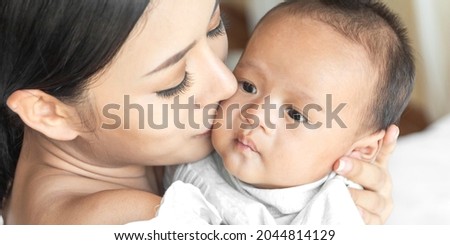 Portrait of enjoy happy love family asian mother playing with adorable little asian baby.Mom kiss with cute son moments good time in a white bedroom.Love of family concept