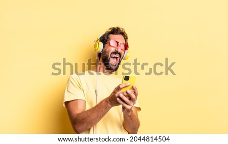 expressive crazy bearded man listening music with headphones and sartphone