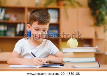 Happy schoolboy sitting at desk, classroom Royalty-Free Stock Photo #2044830188