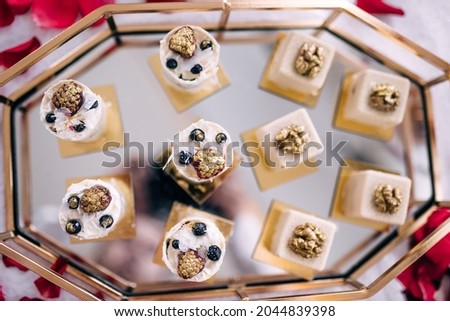 Table with a variety of cakes, muffins, biscuits and cakes with berries and nuts, covered with golden powder