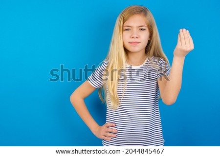 Caucasian blonde kid girl wearing stripped T-shirt against blue wall angry gesturing typical italian gesture with hand, looking to camera