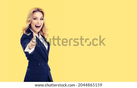 Happy smiling businesswoman in dark blue confident suit, showing thumbs up gesture, isolate on yellow color background. Business success concept. Copy space for text. Female executive person