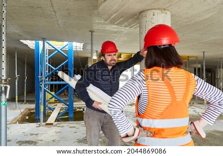 Architect with architectural drawing and construction workers discuss building project on the construction site in the shell