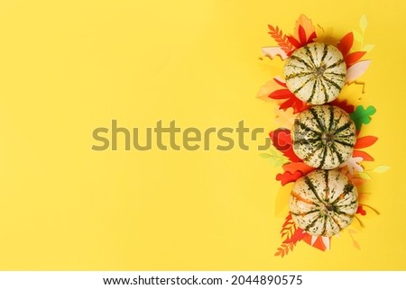 Pumpkins with Autumn paper leaves on yellow background. Thanksgiving greeting card, autumn frame
