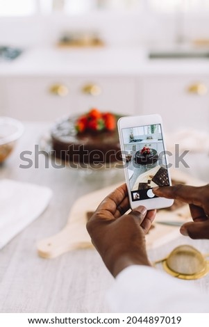 Close-up of a female hands holding mobile phone and taking pictures of cake on kitchen counter. Woman photographing freshly made cake at home.